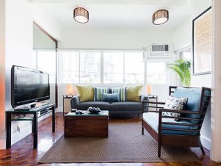 Bright, airy living room interior with modern furnishings, including a gray sofa, patterned chairs, a flat-screen TV