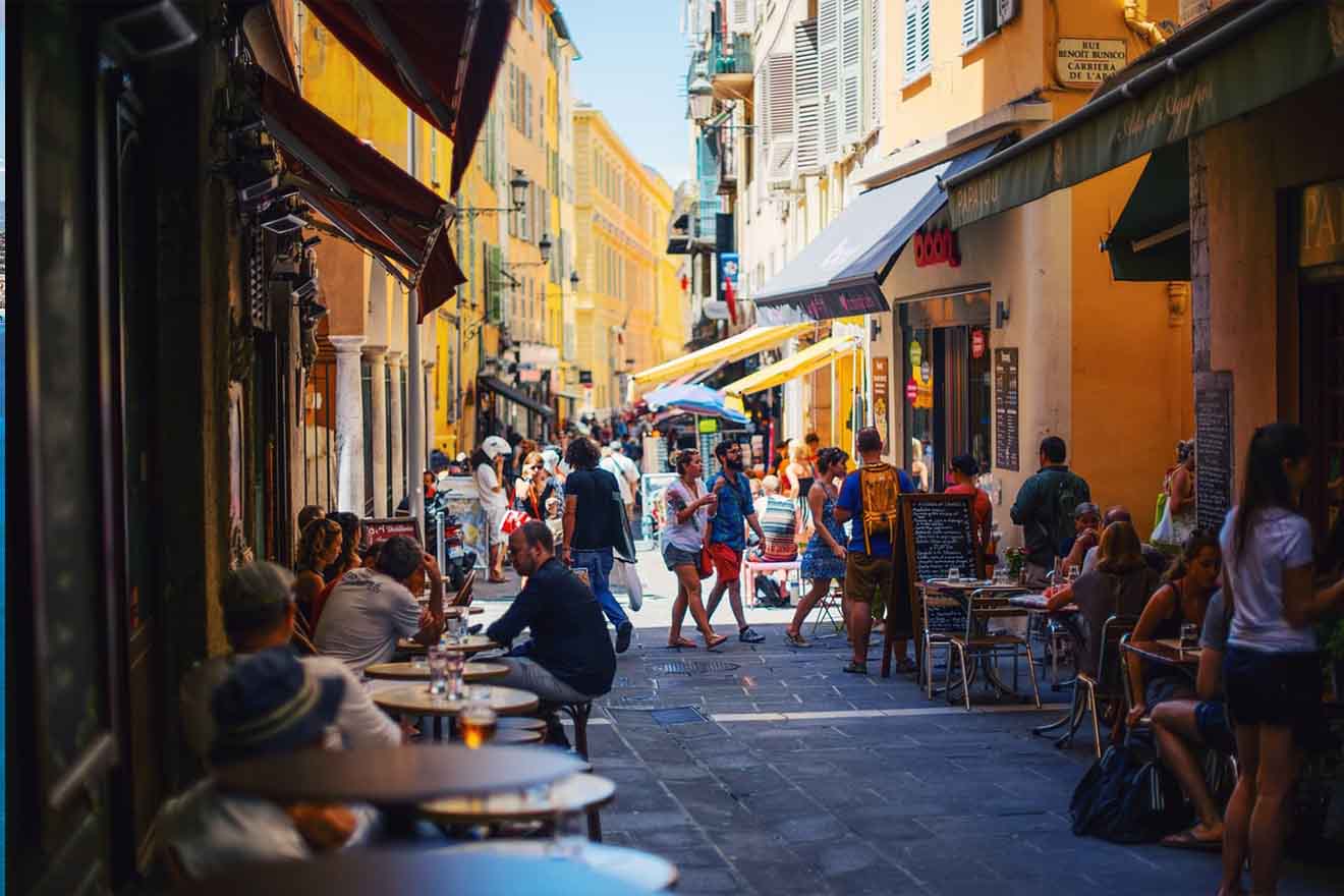Lively street scene in an old town with people dining at sidewalk cafes, nestled between traditional ochre buildings under a bright blue sky