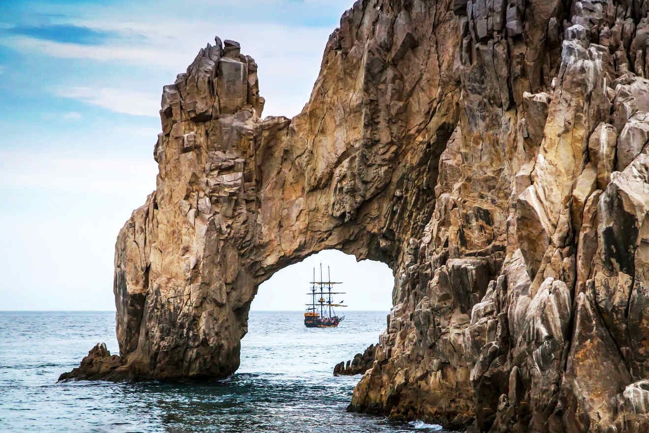 Majestic natural rock arch in the ocean with a vintage sailing ship visible through the opening.
