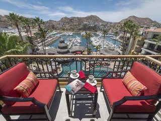 Balcony view overlooking a marina filled with boats, surrounded by a quaint town and hills in the distance, with a table set for two.