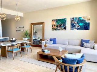 Modern living room with a sectional sofa, wooden furniture, and wall art of aerial beach views, in a contemporary home.