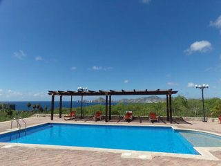 Outdoor pool with ocean view, flanked by wooden pergola and lounge chairs, under a clear blue sky.