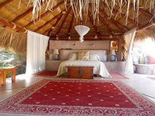 Traditional thatched-roof bedroom with a rustic charm, featuring a large bed and vibrant red area rug.