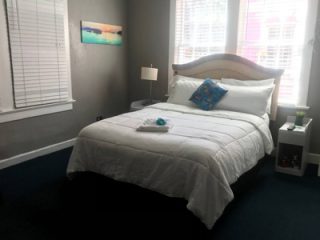 Simple yet elegant bedroom with white bedding, a single aquatic-themed cushion, and minimalist decor, bathed in natural light.