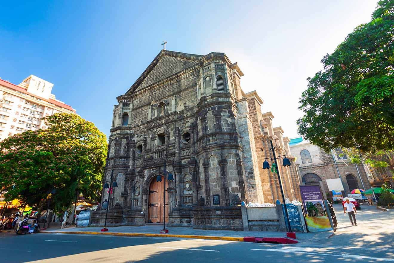 Historic stone facade of the San Agustin Church in Manila, with intricate architectural details, under the shade of a large tree on a sunny day