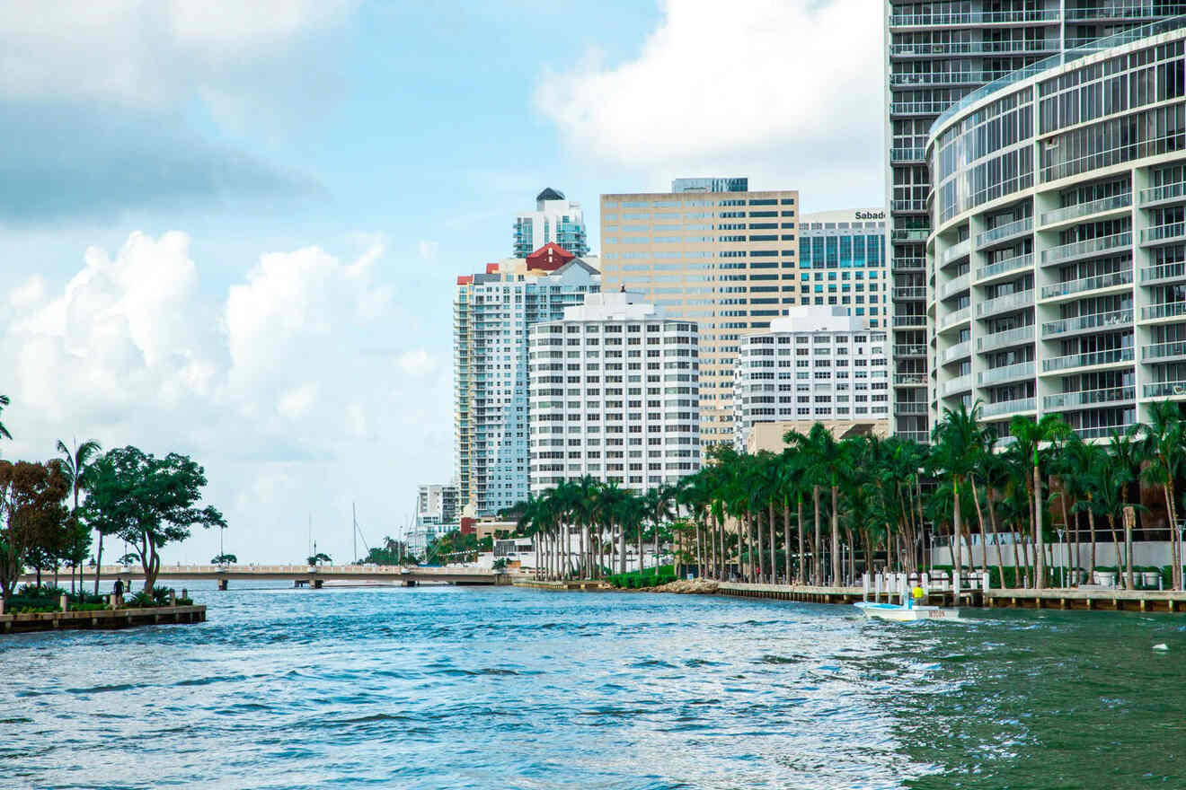 Urban waterfront scene in Miami with palm trees, waterfront buildings, and a cloudy sky.