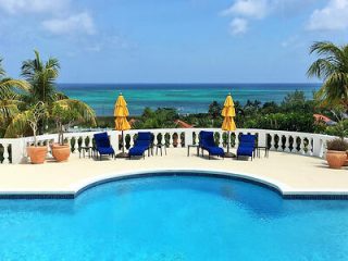 Resort-style outdoor swimming pool with curving edges, surrounded by lounge chairs and umbrellas, overlooking an expansive ocean view.