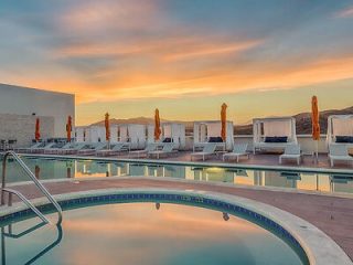 Rooftop pool at dusk with lounge chairs and umbrellas, offering a stunning view of the sky's warm hues.