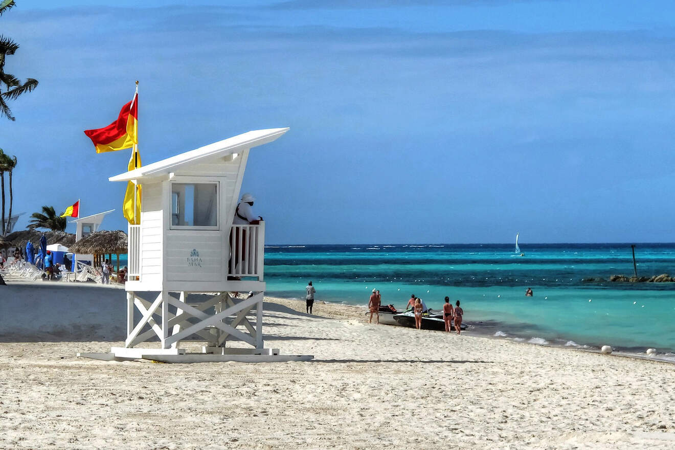 Beach scene in Nassau with a lifeguard stand flying red and yellow flags, overseeing a lively beach with visitors and clear turquoise waters.