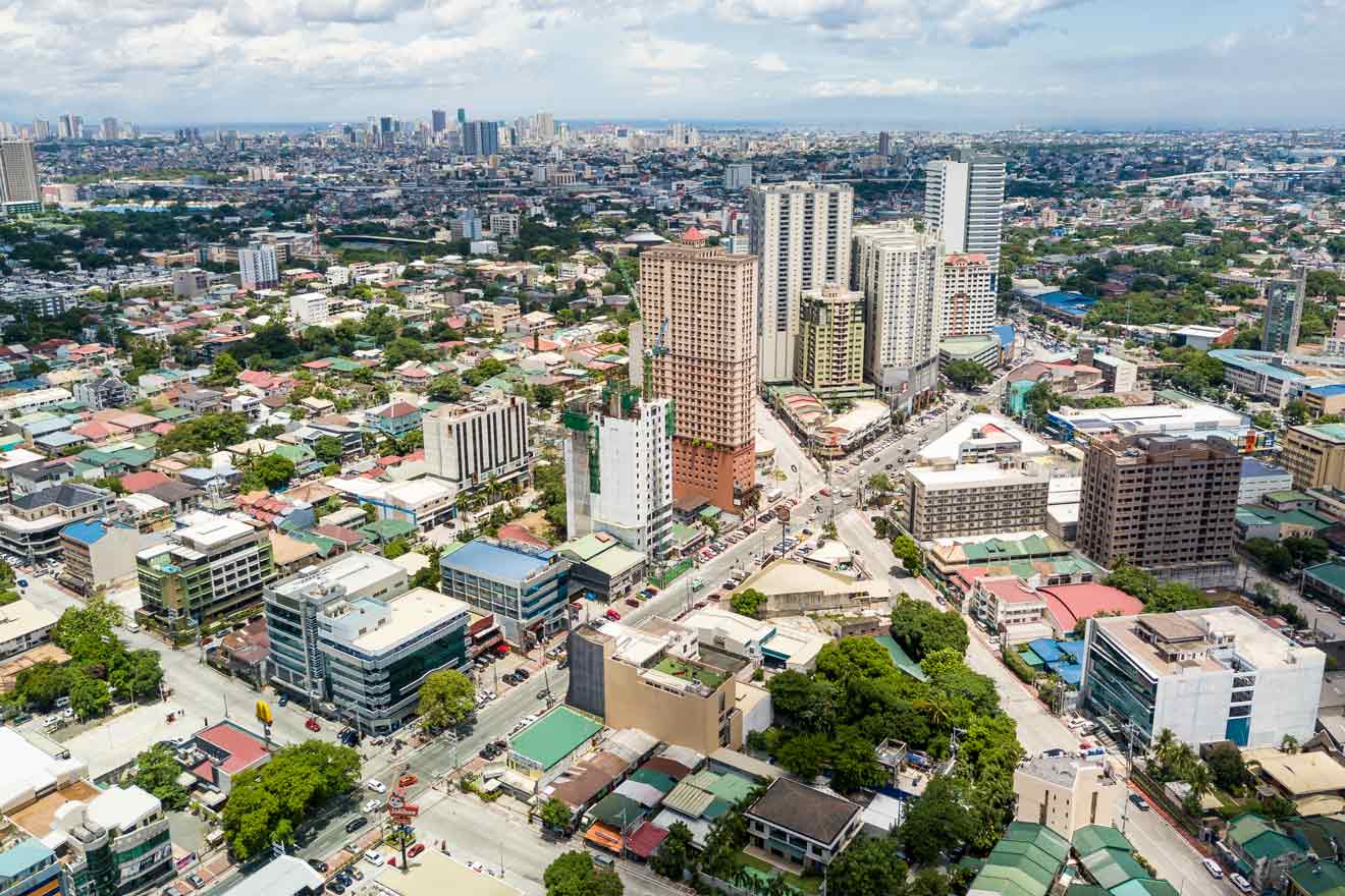 Aerial view of a dense Manila neighborhood with mixed residential and commercial buildings, intersecting roads, and scattered greenery on a sunny day.