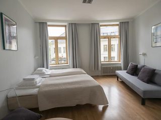 Spacious and bright hotel room with a large bed, grey curtains, and a grey sofa by the window offering a view of the city street.