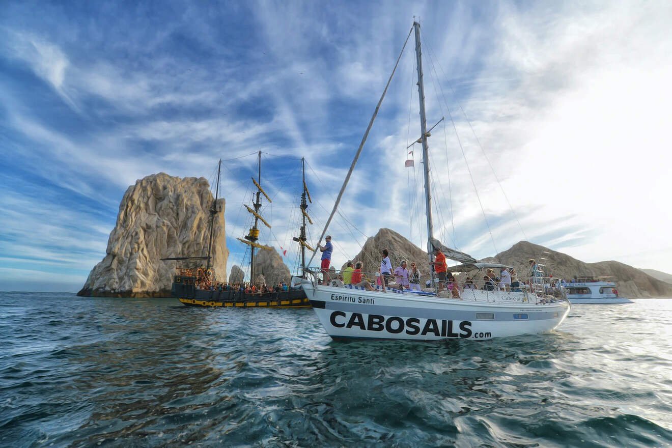 Tourists enjoying a sailboat excursion near the iconic rock formation of Los Cabos, with clear skies.