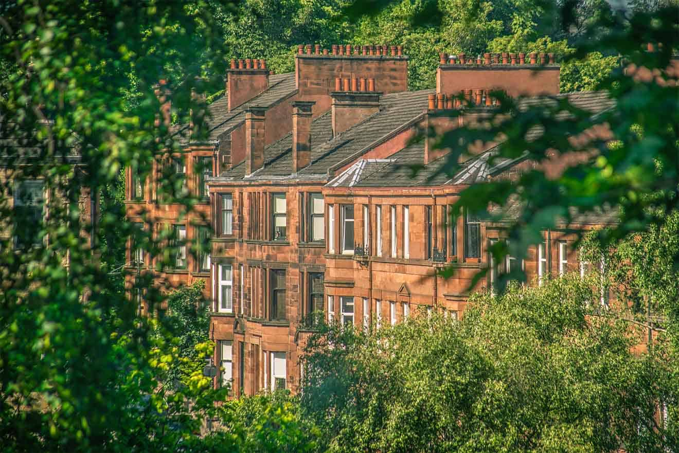 The distinguished Kelvingrove Art Gallery and Museum in Glasgow, presented in warm sandstone against a blue sky, with people enjoying the manicured lawns