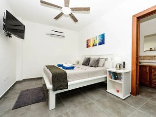 Minimalistic and neat bedroom with a large bed, air conditioning, and a view into the bathroom, reflecting a modern tropical stay.