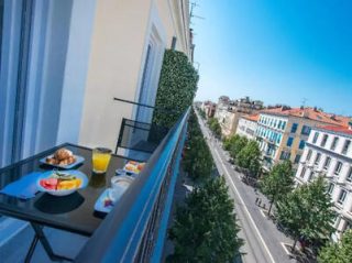View from a balcony with a breakfast spread overlooking a tree-lined street in Nice