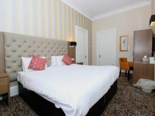 Hotel room with a large bed, tufted headboard, and striped wallpaper.