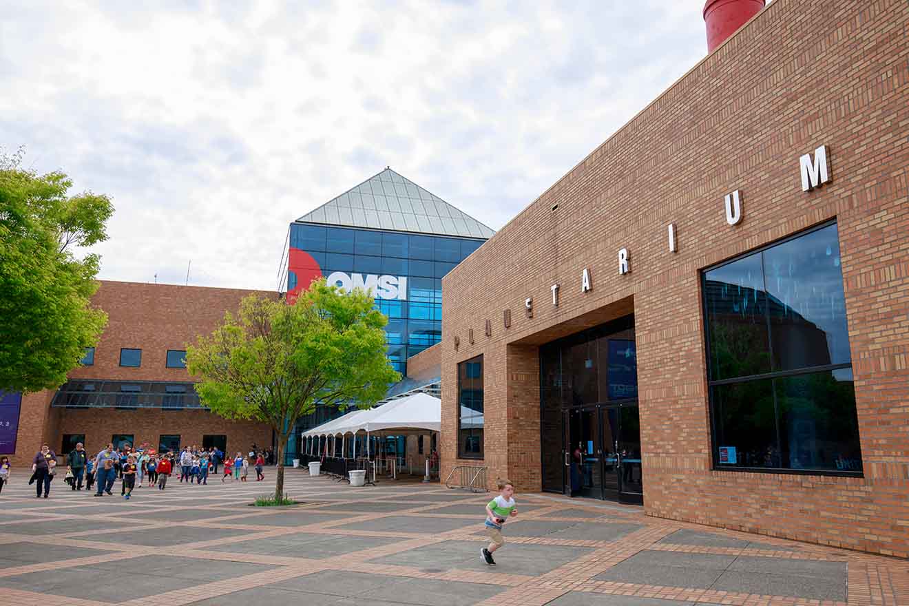 Exterior view of the Oregon Museum of Science and Industry (OMSI) with visitors gathering at the entrance on a cloudy day