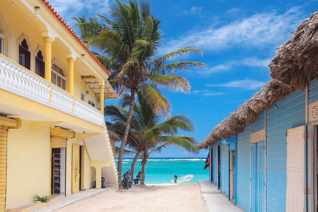 Quaint yellow beachfront building with palm trees and a clear path leading to the vibrant blue sea.
