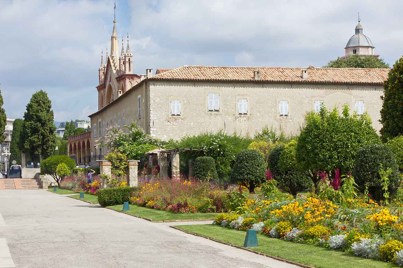 Manicured garden with vibrant flowers and greenery in front of an historic, sandy-colored building with a backdrop of clear blue skies