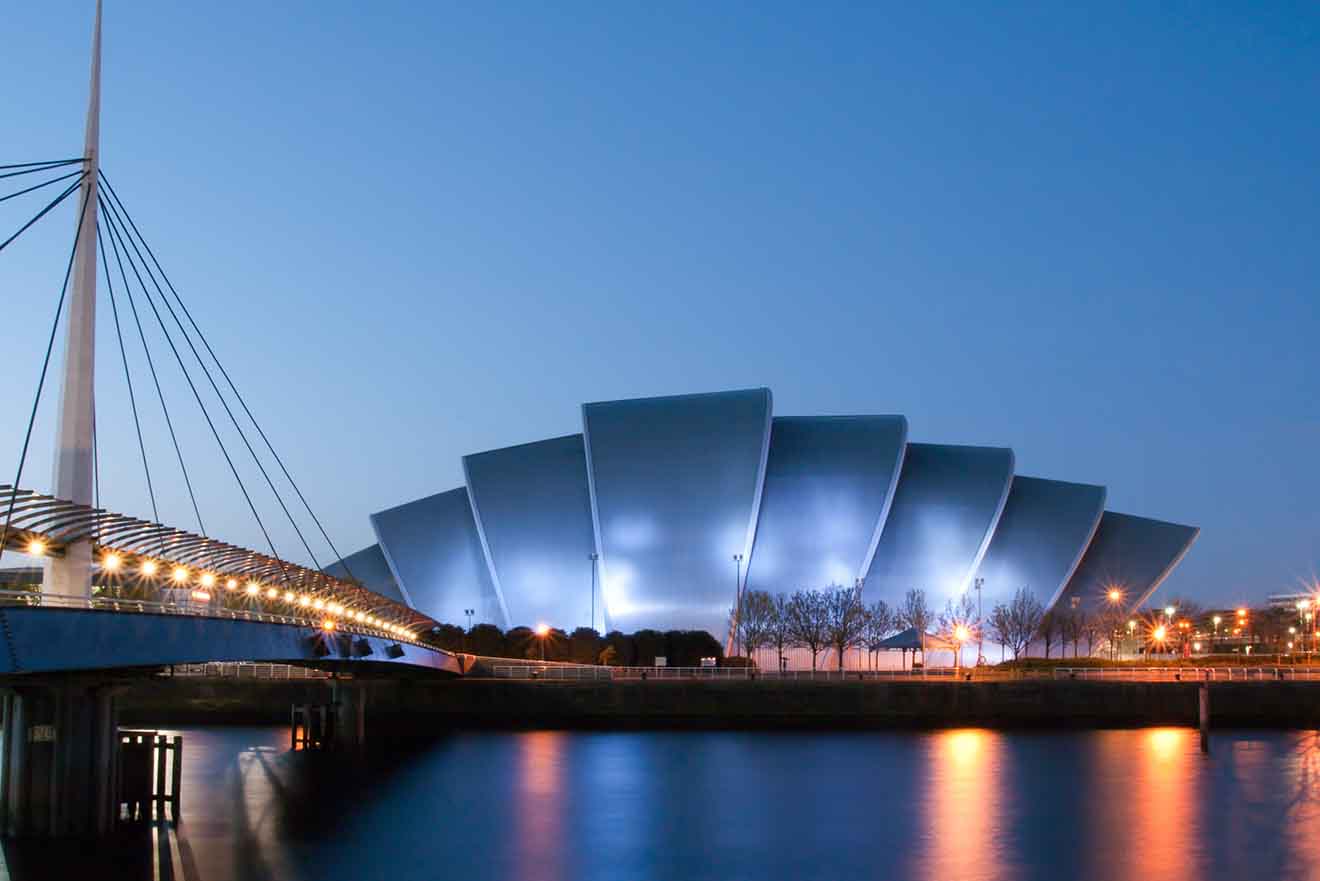 Twilight view of the Clyde Auditorium, affectionately known as 'The Armadillo', in Glasgow, with its unique shell-like architecture illuminated and reflected in the calm waters of the River Clyde.