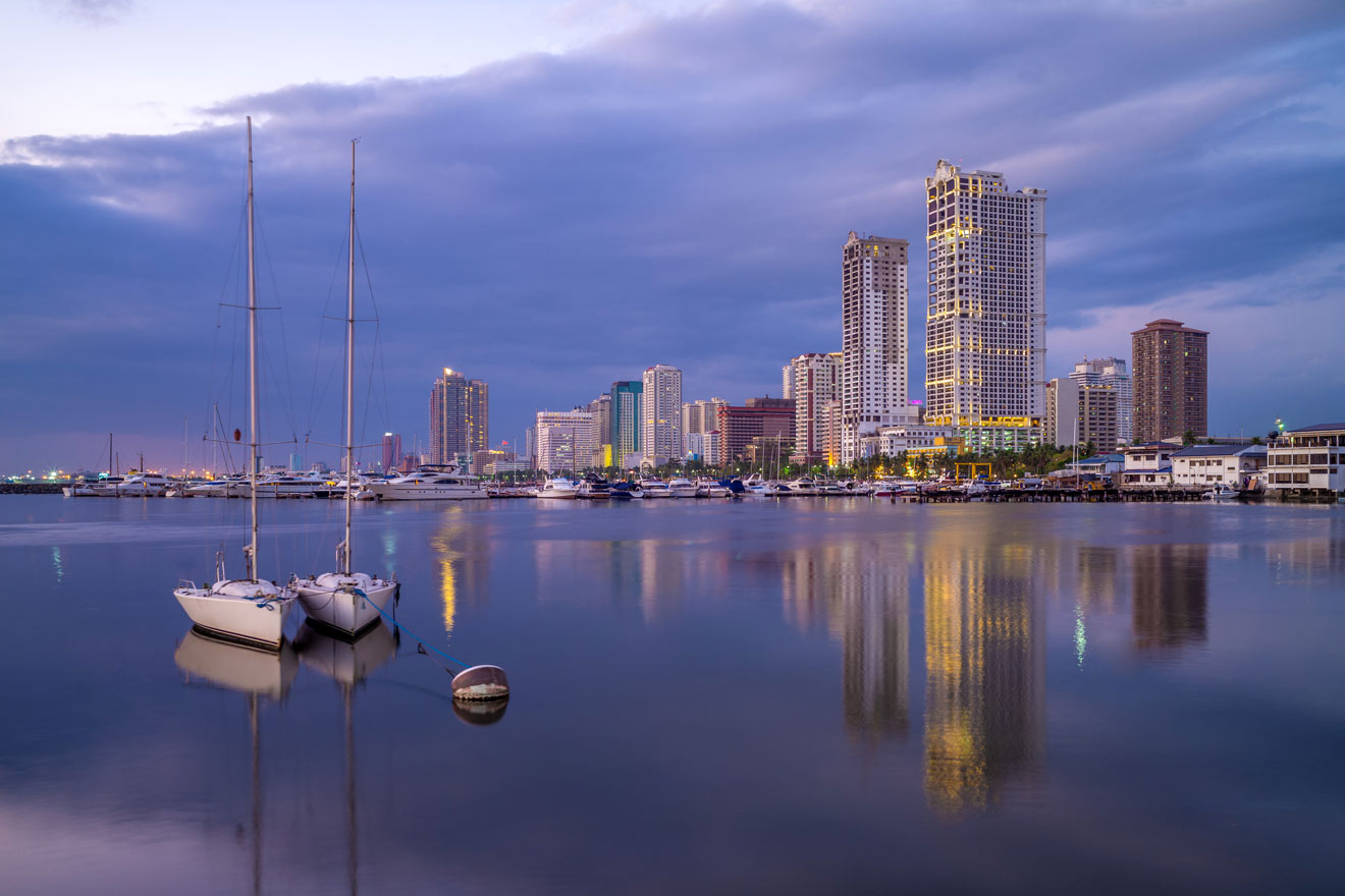 Tranquil twilight scene at Manila Bay with moored sailboats and a silhouette of the city skyline reflecting on calm waters