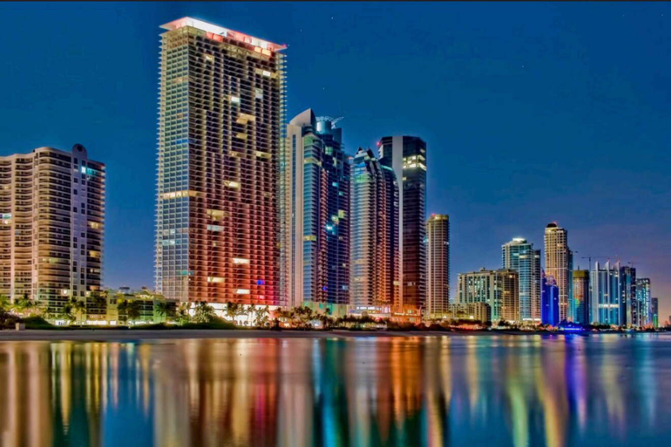 Night view of Miami's glowing skyline reflected on the water, showcasing high-rise buildings and vibrant city lights.