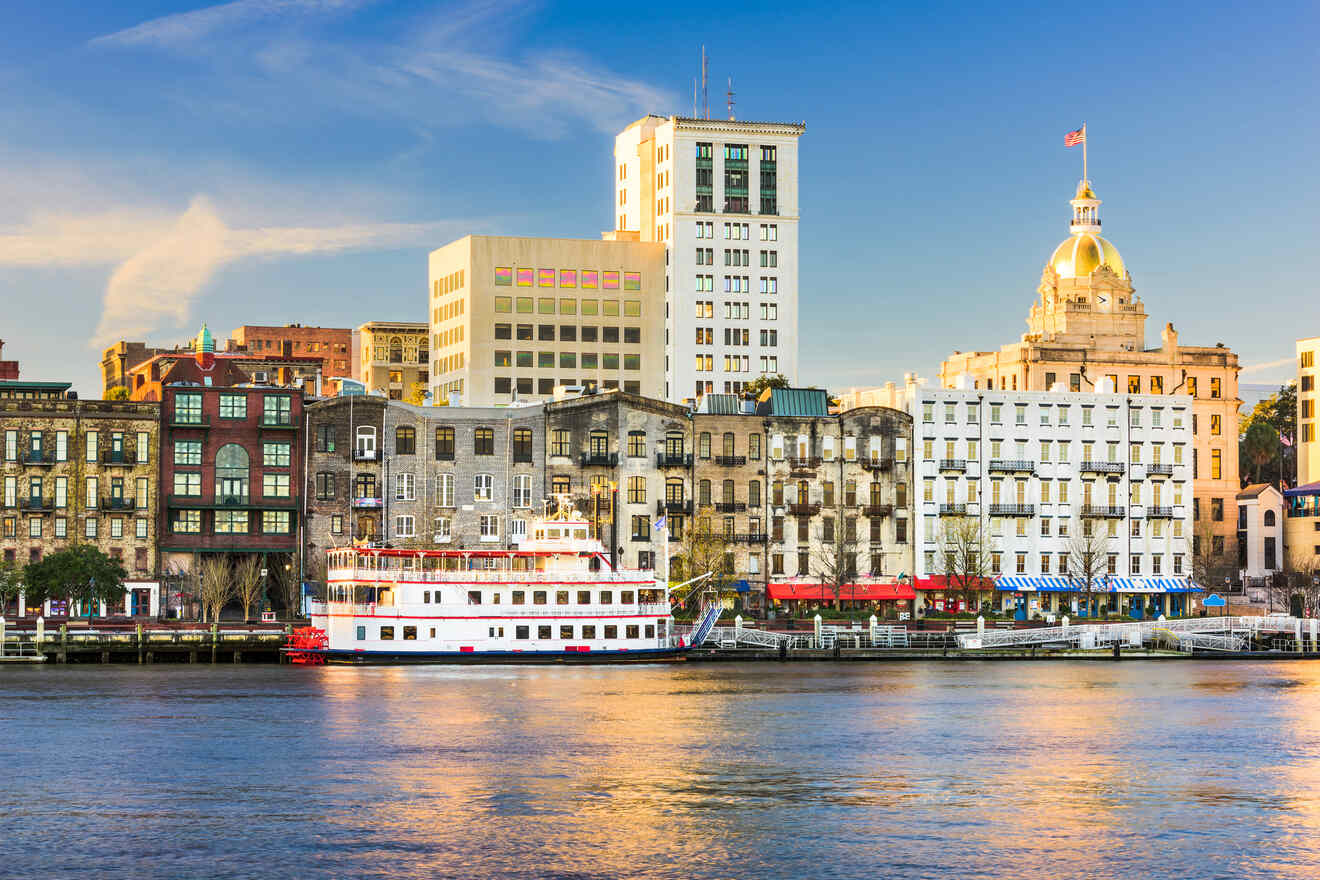 Waterfront view of Savannah's historic River Street with a passing tour boat and a clear blue sky backdrop.