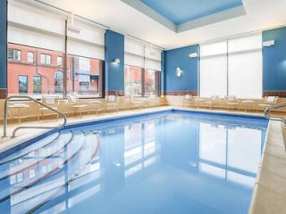 Indoor swimming pool in a hotel with large windows, multiple chairs, and a blue-tiled pool