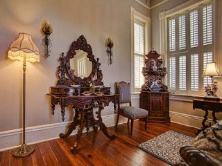 Vintage vanity dresser with ornate mirror and classic wooden furniture in a bright room with plantation shutters