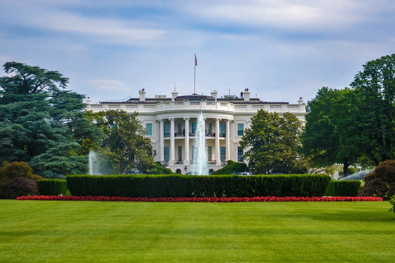 The White House viewed across the lush South Lawn with a water fountain in the foreground, under a clear sky.
