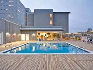 Rooftop swimming pool at dusk with modern deck chairs and city buildings in the background, offering urban relaxation.