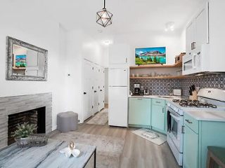 Modern, compact kitchen with teal cabinetry, white appliances, and a rustic wooden floor