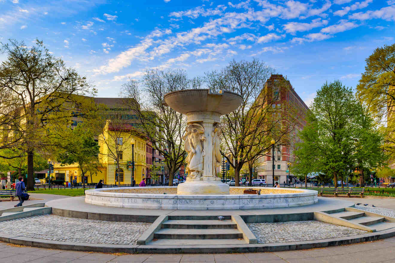 A historic fountain at Dupont Circle in Washington D.C., with surrounding park benches and the early signs of spring in the trees.
