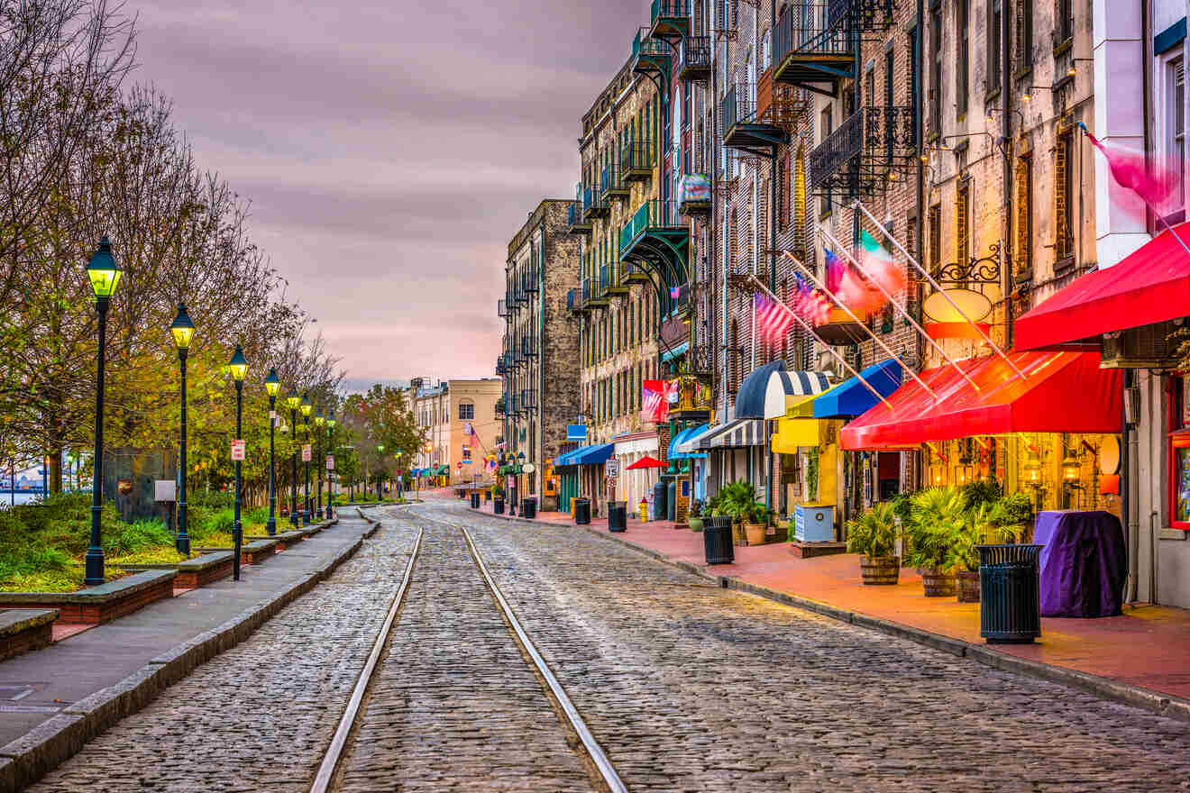 Twilight descends on a historic cobbled street lined with vintage lamp posts and vibrant storefronts with colorful awnings, capturing the quaint charm of an old city district.