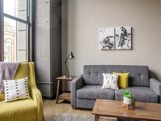 Cozy living room with a gray sofa, yellow armchair, wooden coffee table, and abstract art on the wall