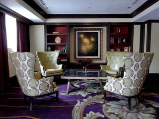 An elegant sitting area with two patterned armchairs, a glass coffee table, and a decorative sunburst mirror on the wall in a luxurious interior setting.