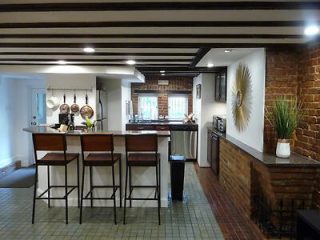 A spacious kitchen featuring a large island with bar stools, brick walls, and modern appliances, with natural light coming through a window in the background.