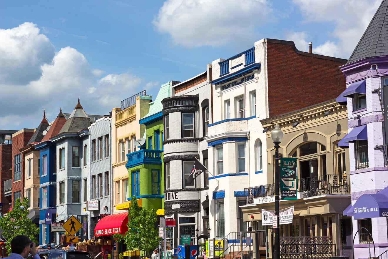 A vibrant streetscape of Adams Morgan with colorful row houses and assorted businesses under a clear blue sky.
