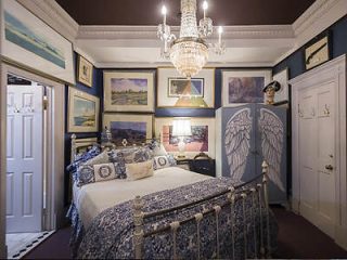 A sophisticated bedroom decorated with angel wing bedposts, framed artwork, and a luxurious chandelier, offering a mix of classic and whimsical styles.