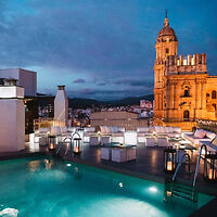 Evening ambiance at a rooftop pool with a view of a historic cathedral's illuminated towers in the backdrop