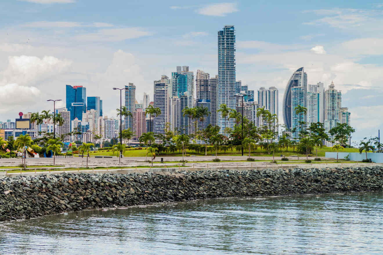 Panoramic view of Panama City skyline with modern high-rise buildings and lush greenery in the foreground, under a cloudy sky