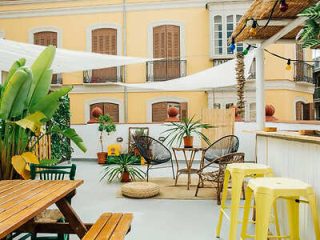 Chic and airy urban terrace decorated with white drapery, tropical plants, and modern outdoor furniture.