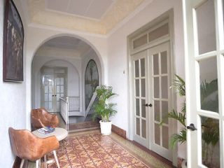 Elegant interior hallway featuring vintage patterned floor tiles, white walls, a brown leather chair, and natural light filtering through French doors