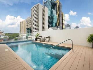 Rooftop swimming pool on a sunny day with wooden decking, lounge chairs, and a view of Panama City's skyscrapers in the background