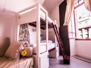 Cozy hostel room with bunk beds, a small seating area, and a window in Lisbon