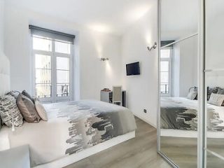 Chic bedroom with a large bed, mirrored closet doors, and natural light in a Lisbon home.