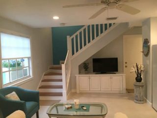 Bright living space with a teal accent wall, understated white furniture, and a staircase leading to the upper level, offering a modern and open feel