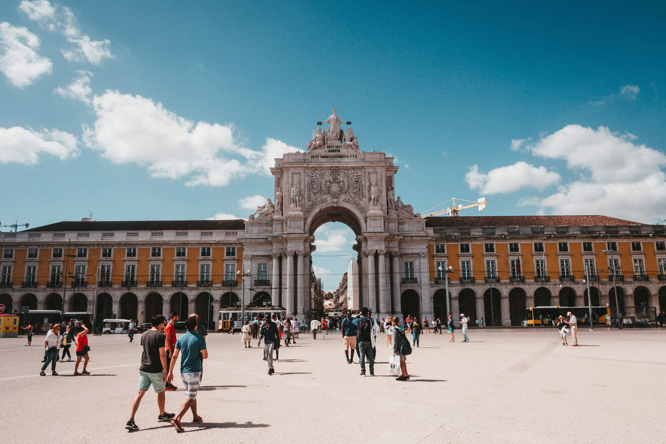 Crowded Praça do Comércio in Lisbon, showing people walking across the spacious square with the iconic Rua Augusta Arch in the background