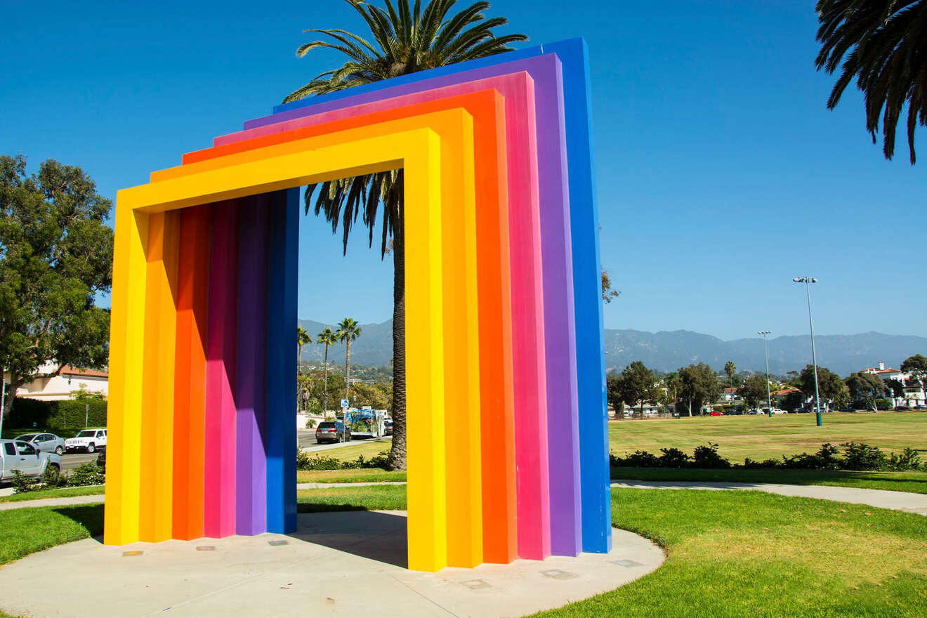 Vibrant multi-colored, geometric archway sculpture set against a backdrop of palm trees and blue sky in Santa Barbara, highlighting the city's creative public art.