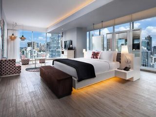 Luxurious bedroom with a large bed, contemporary furnishings, and panoramic windows showcasing an urban skyline at dusk